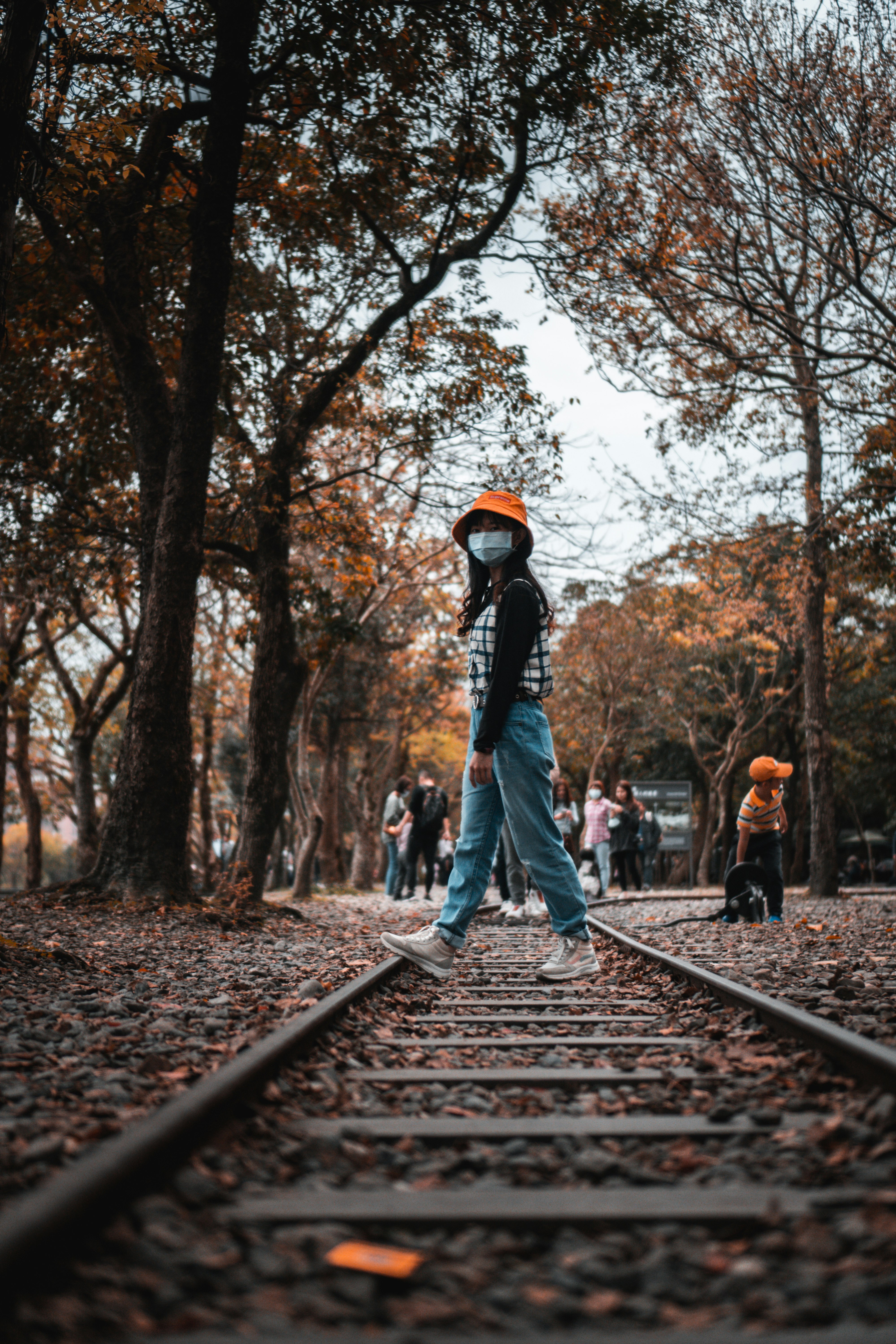 man in black jacket and blue denim jeans walking on train rail during daytime